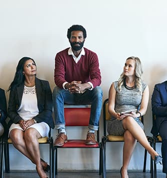 man sitting on the top of the back of a chair while others next to him sit on the chair seat