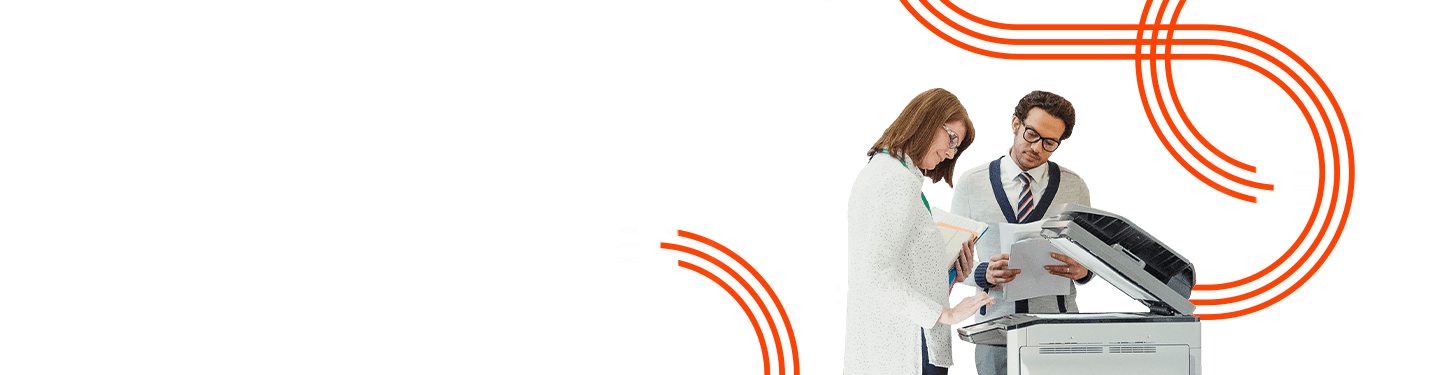 Two educators review documents next to a photocopier in a school hallway, illustrating efficient printing solutions for K-12 budgets.