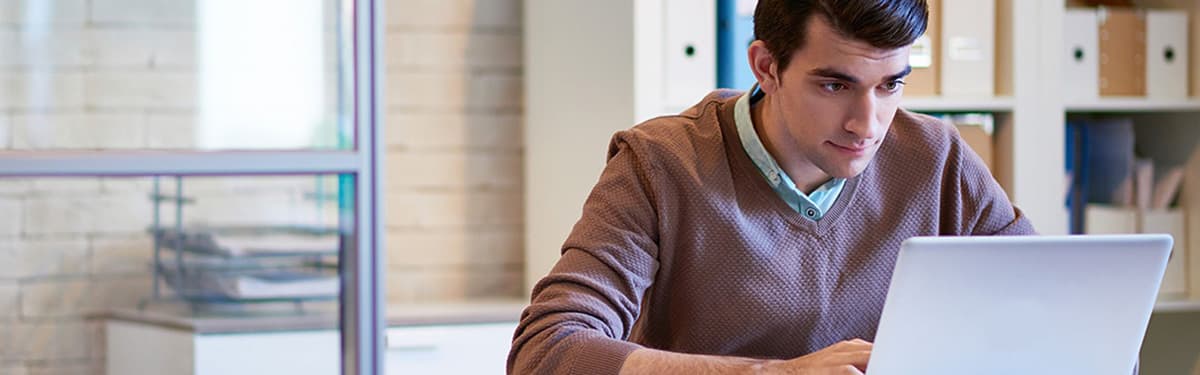 Photo of a man wearing a purple sweater working at his laptop.